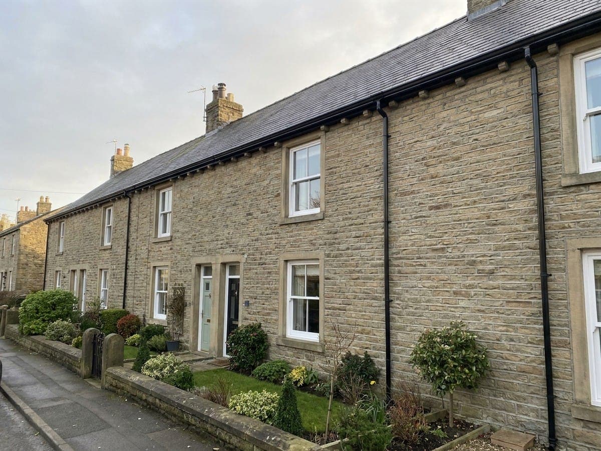 Clean, intact black guttering and downpipe running along the front of a tidy stone terrace kept clear year on year